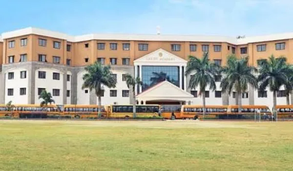 Christ Academy ICSE School Christ Academy ICSE School, Bangalore — long ochre school building with a gabled entrance porch and a line of school buses drawn up in front of the playing field