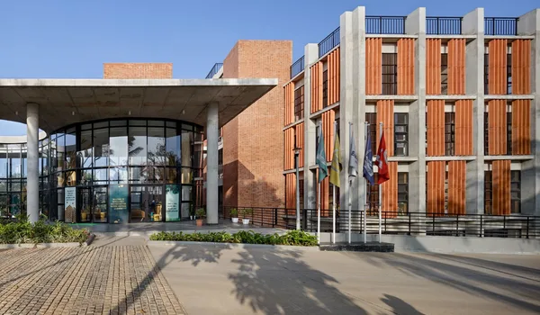 EuroSchool Bannerghatta EuroSchool Bannerghatta, Bangalore — brick and timber-louvred campus block with a curved glazed entrance canopy and a row of flagpoles