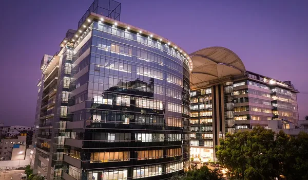 Kalyani Magnum Tech Park Kalyani Magnum Tech Park, Bangalore — curved glass office building with lit floors at dusk and a canopied block alongside