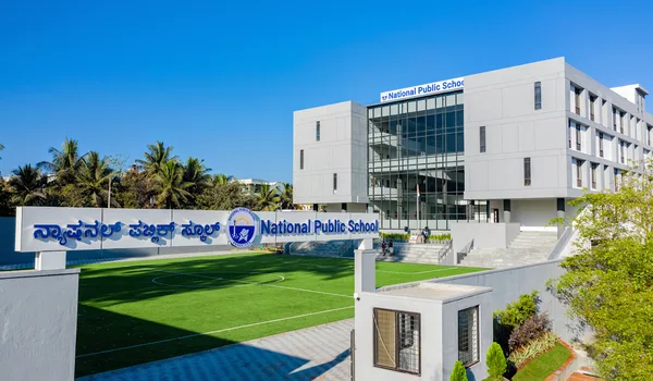 National Public School (NPS), JP Nagar National Public School, JP Nagar, Bangalore — the school name in Kannada and English on the boundary wall beside the turf field, with the classroom block behind