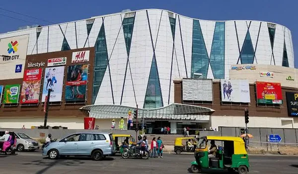 Nexus Vega City Mall on Bannerghatta Road near Nambiar Beverly Green, a white curved-glass mall with Lifestyle, SPAR and H&M signage and traffic on the road in front